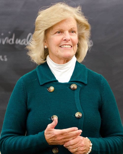 Dr. Anne Hendershott in a blue blouse standing in front of a blackboard.
