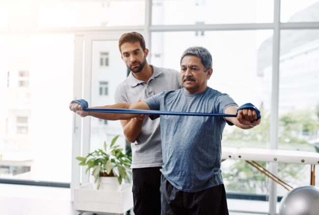 Male physiotherapist helping a male patient with movement exercises at a clinic