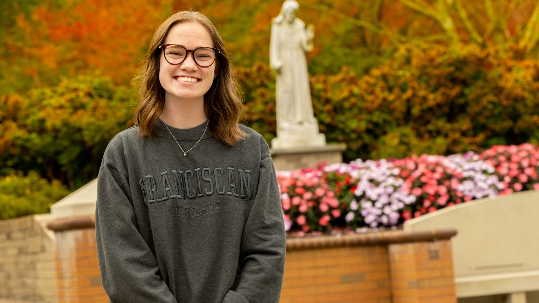 Student smiling in front of the St. Francis Statue