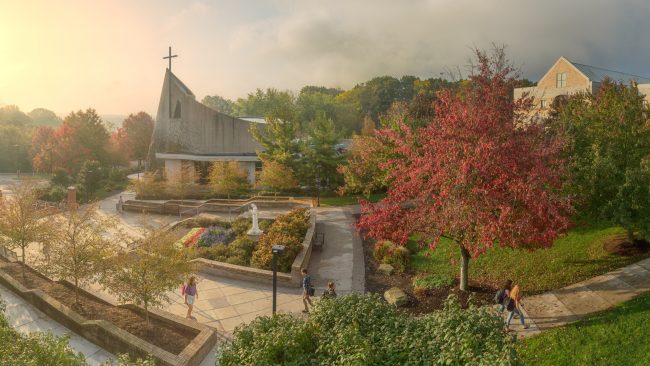 The facade of the Steubenville chapel in the background of a spring scene with students walking on sidewalks.