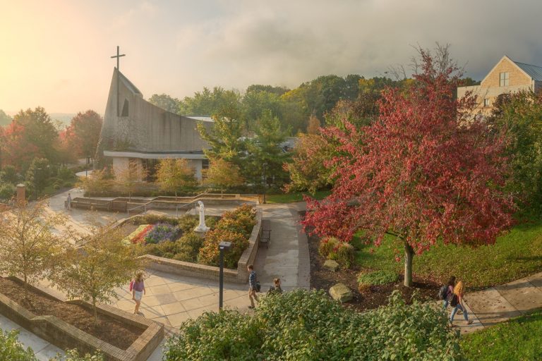 The facade of the Steubenville chapel in the background of a spring scene with students walking on sidewalks.