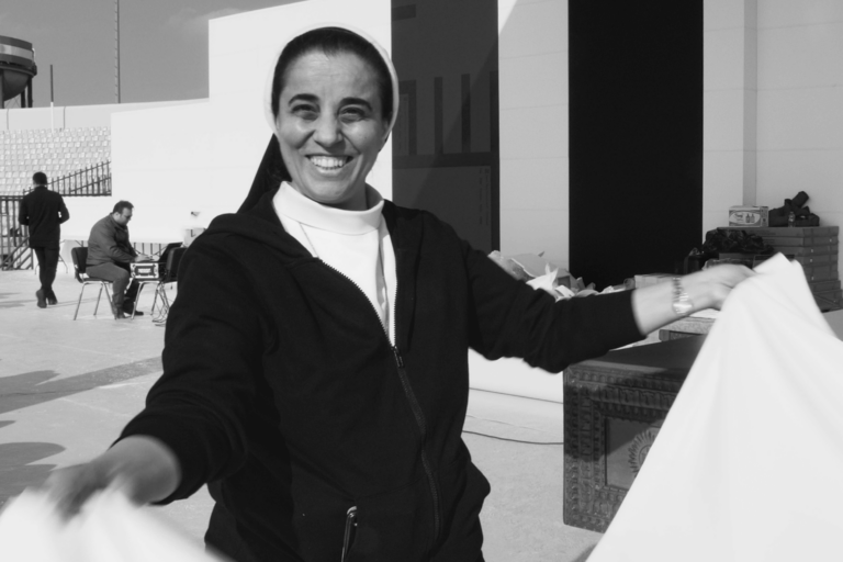Black and white photo of a nun outside with a table cloth in her hand.