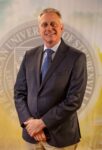 Dr. John Bergsma standing in front of the Franciscan University of Steubenville seal.