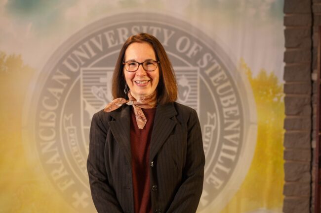 To Web – Dr. Monica Anderson FEB2025 -2533 Dr. Monica Anderson standing in front of a university seal.