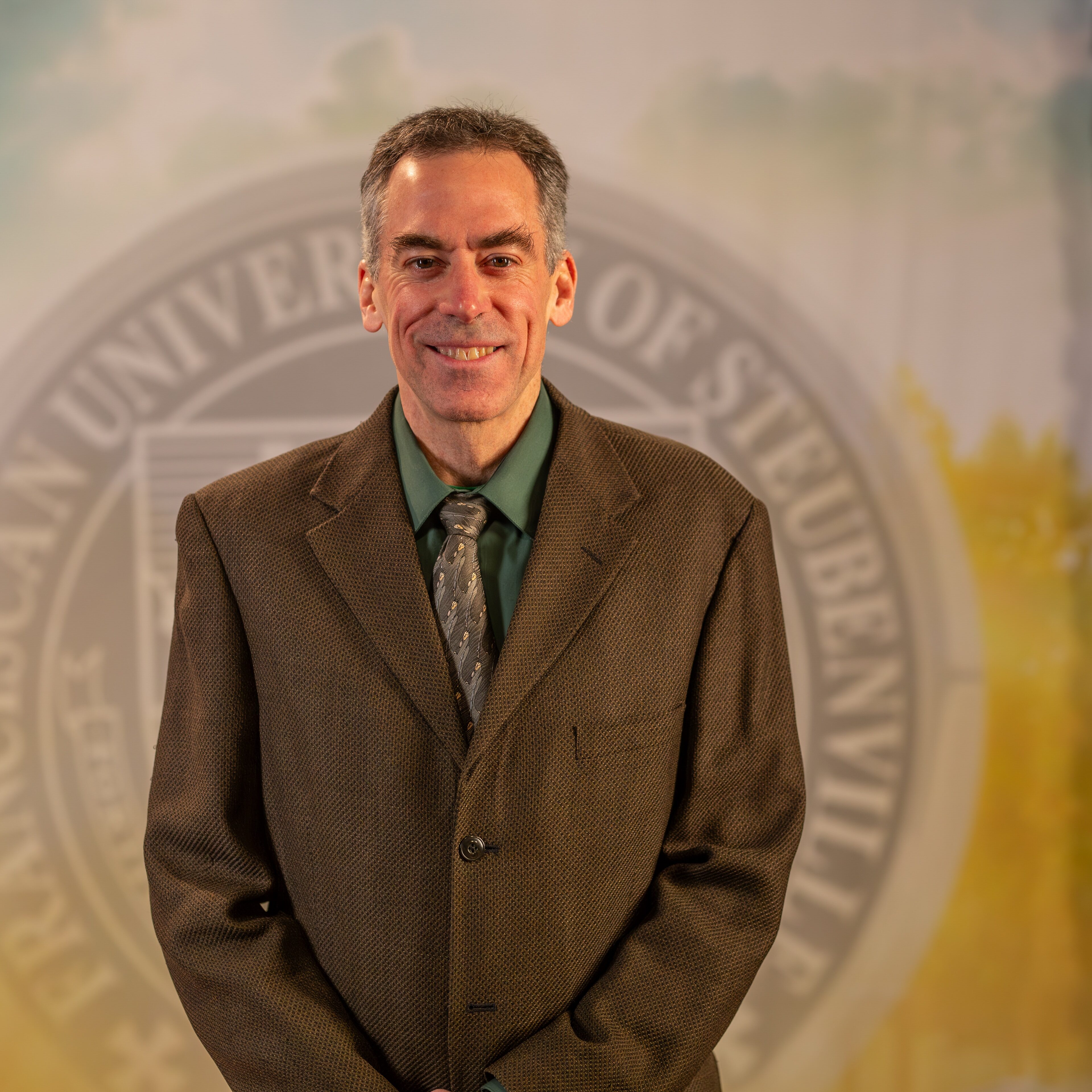 Dr. Ron Bolster standing in front of the Franciscan University of Steubenville seal.