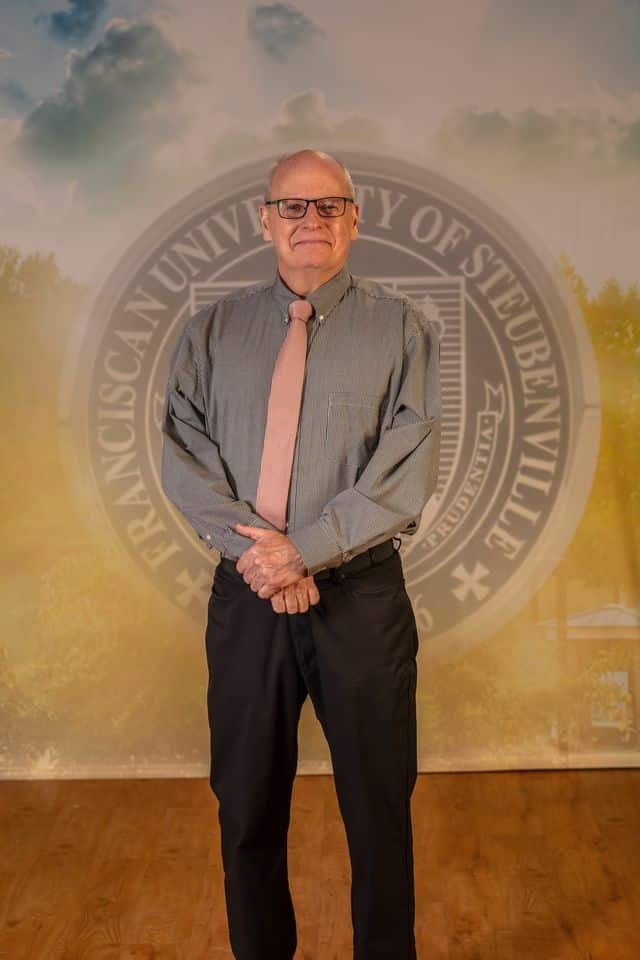 Dr Timothy Williams 2025 Dr. Timothy Williams in professional wear standing in front of the university seal.