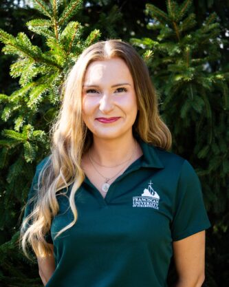 Megan Case Admission Counselor Outdoor portrait of Megan Case wearing a green polo embroidered with the Franciscan University of Steubenville logo.