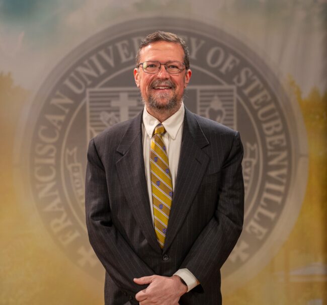 Faculty portrait of Dr. Michael Sirilla standing in front of the Franciscan University of Steubenville seal.