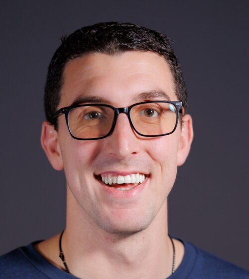 John Caliguire with a blue shirt in front of a dark gray background.