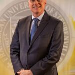Dr. John Bergsma standing in front of the Franciscan University of Steubenville seal.