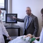 Professor Antinone teaching two students over nursing dummy