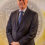 Dr. John Bergsma standing in front of the Franciscan University of Steubenville seal.