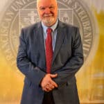 Dr. Petroc Willey standing in front of a university seal.
