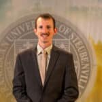 Taylor Caputo standing in front of the Franciscan University of Steubenville seal.