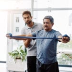 Male physiotherapist helping a male patient with movement exercises at a clinic