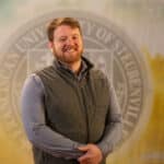Matthew Cahill standing in front of a college seal.